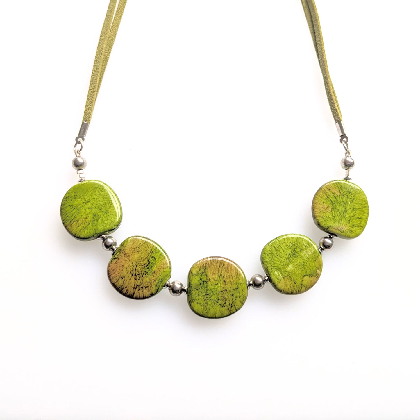 A crescent style necklace of resin pebble-shaped beads green mustard.  Set on a faux suede cord with a T-bar clasp at the back