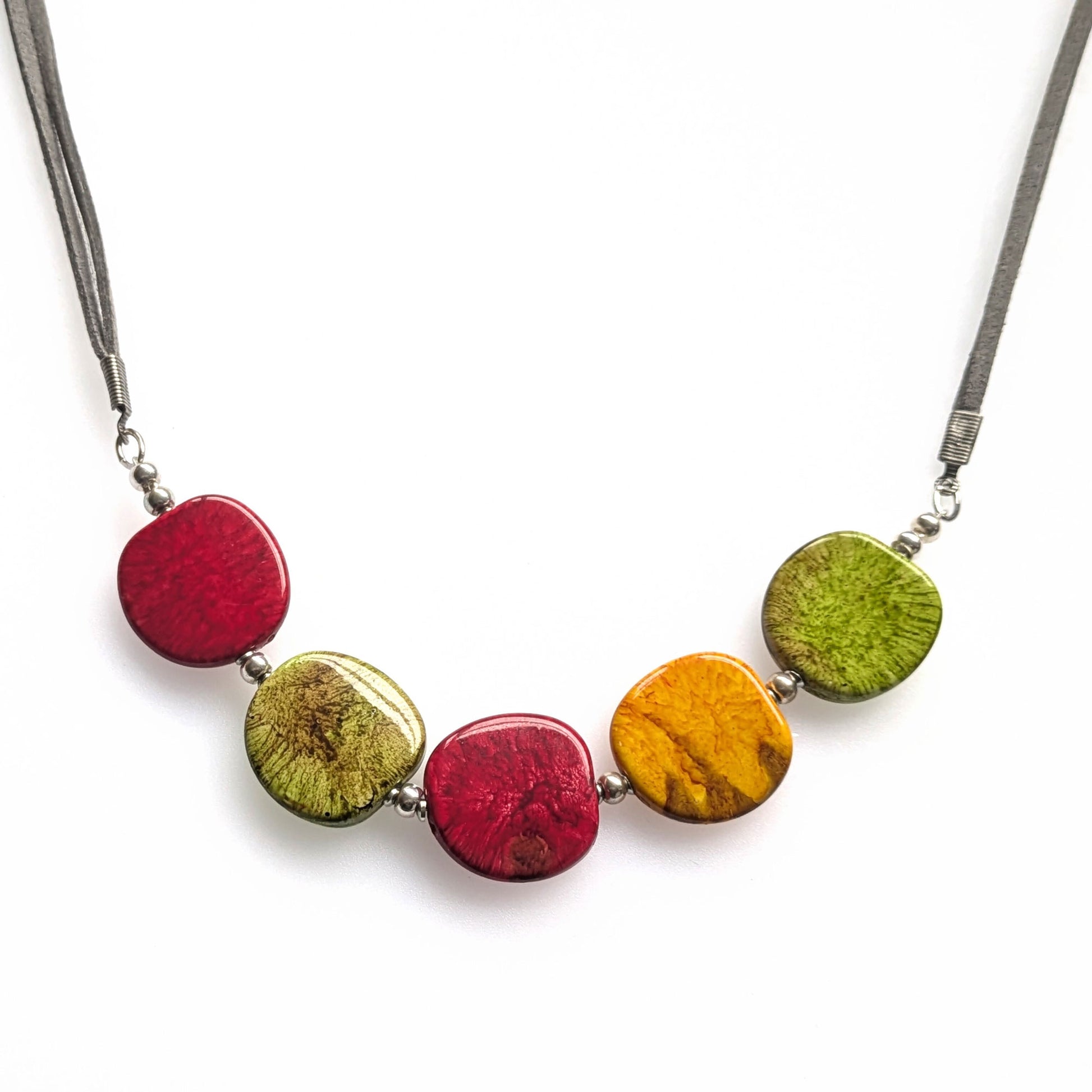 A crescent style necklace of resin pebble-shaped beads in red, green and mustard.  Set on a faux suede cord with a T-bar clasp at the back