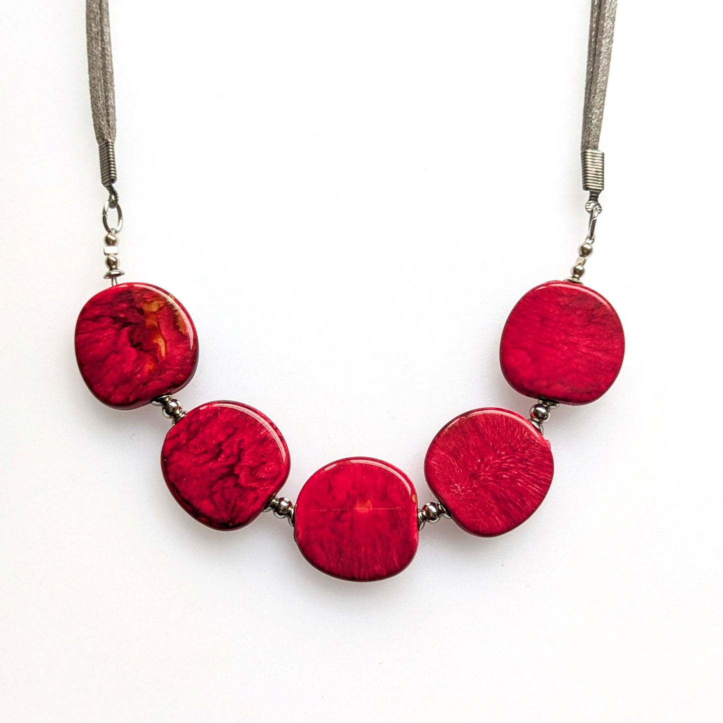 A crescent style necklace of resin pebble-shaped beads in red.  Set on a faux suede cord with a T-bar clasp at the back