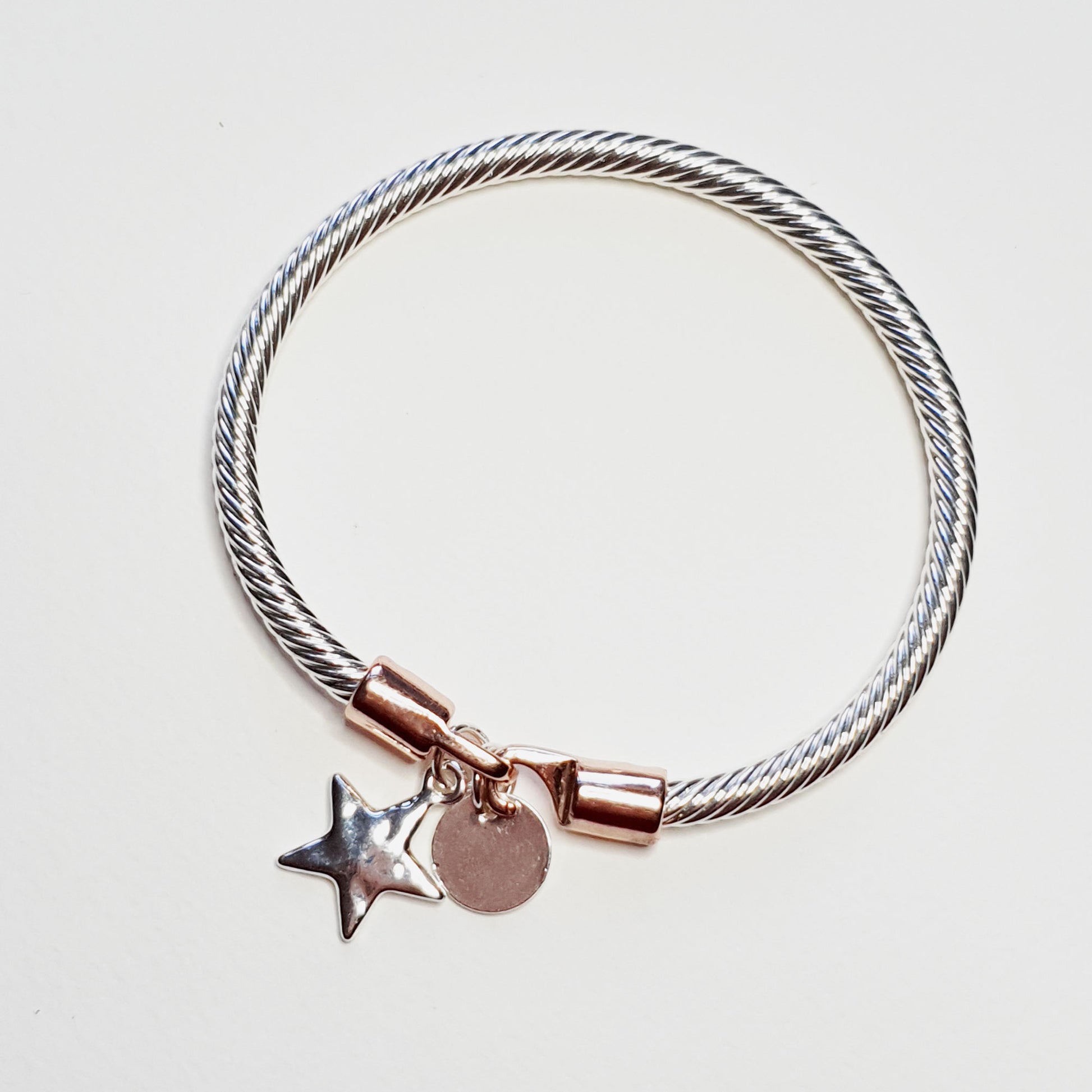 Twisted rope effect silver plated bangle with a charm on the rose gold plated clasp