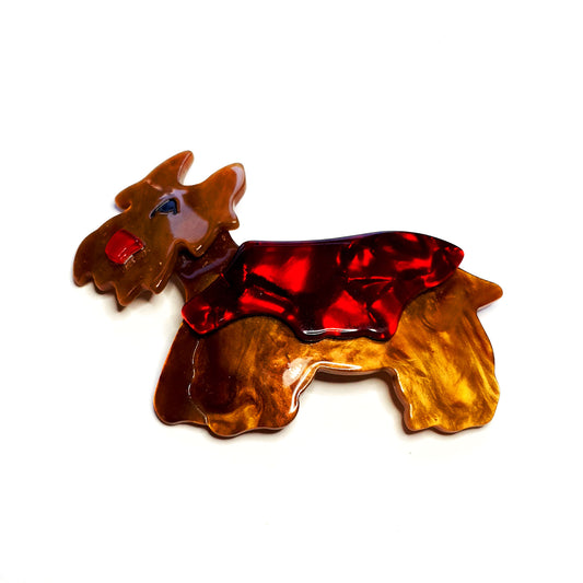A resin scottie dog brooch depicted wearing a red coat.